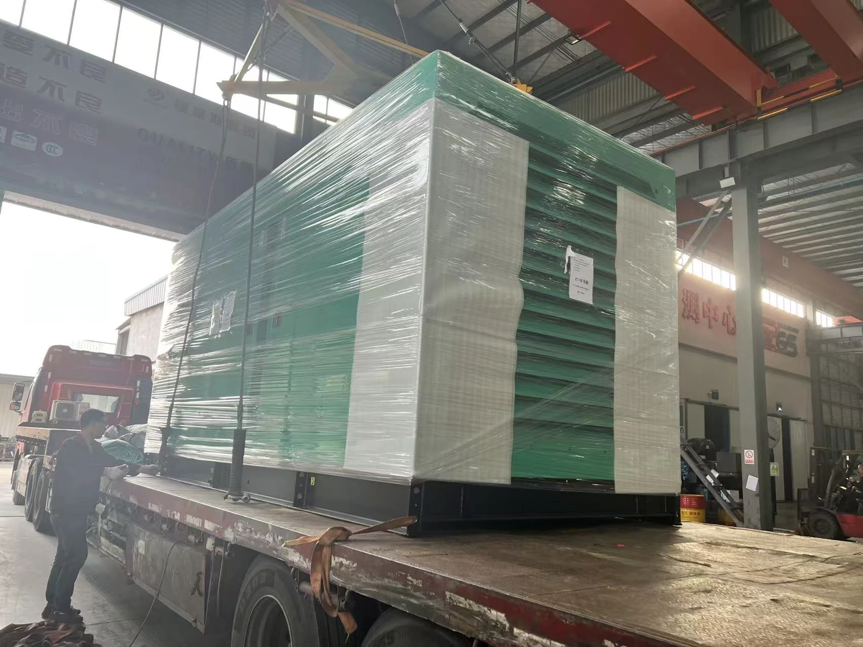 Wrapped enclosed generator unit being loaded onto a flatbed truck at the factory